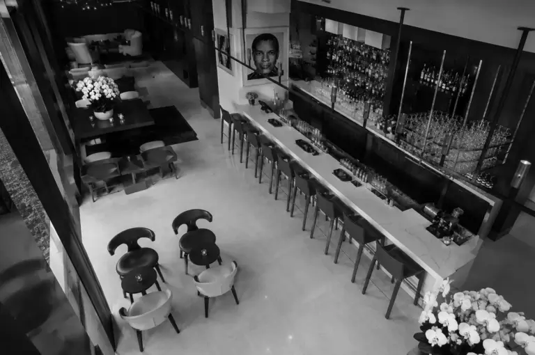 Dimly lit, empty restaurant interior with a long bar, wooden chairs, and hanging spherical lights. The atmosphere is modern and elegant.