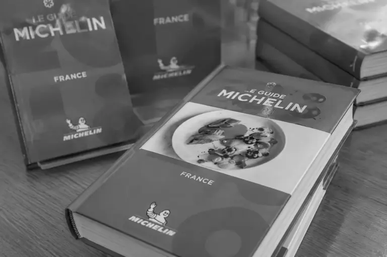 Black and white photo of Le Guide Michelin France books stacked on a wooden table