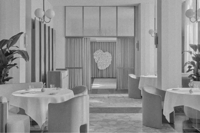 A monochrome image of a minimalist, elegant restaurant interior. Round tables with white tablecloths, modern chairs, large leafy plants, and spherical light fixtures create a serene, sophisticated ambiance. A textured art piece resembling a heart is centered on the far wall.