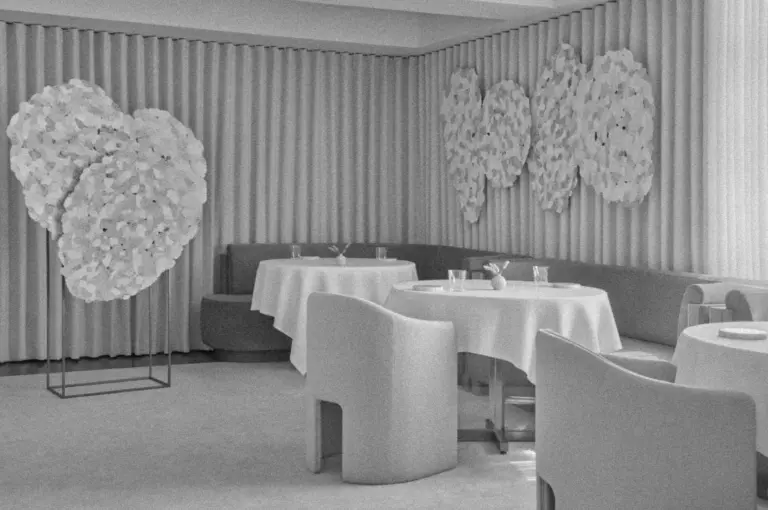 Sleek restaurant interior in black and white, featuring round tables with white tablecloths, modern chairs, and artistic wall decor set against panel curtains.