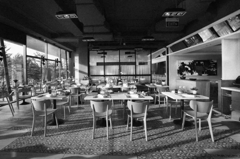 Modern restaurant interior in black and white, with empty tables and chairs. Large windows let in natural light, creating a serene ambiance.