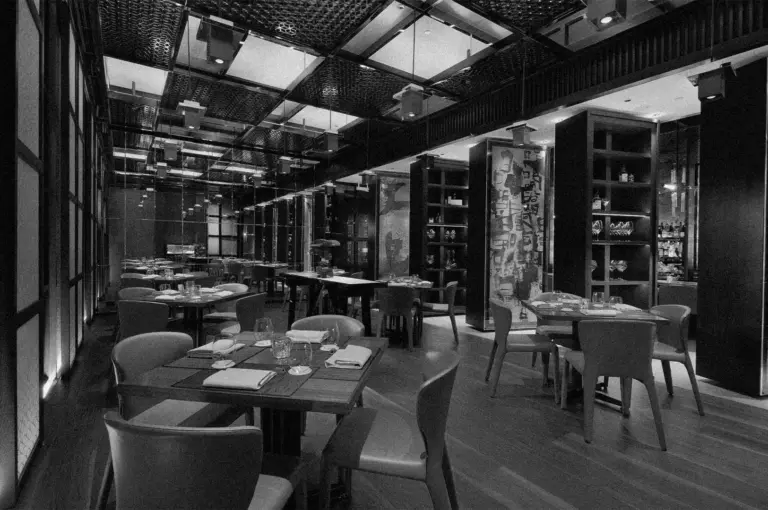 Elegant restaurant interior in black and white. Features sleek tables set with glasses and napkins, dim lighting, modern decor, and a sophisticated ambiance.
