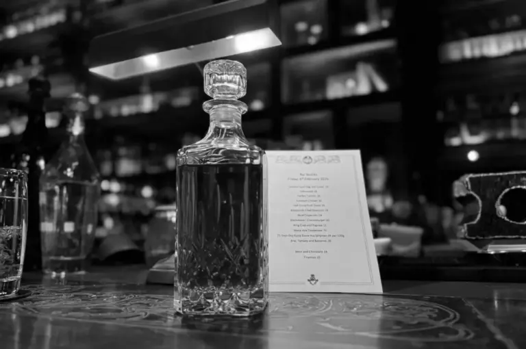 Crystal decanter and bar menu on counter with wine cellar bottles displayed in background