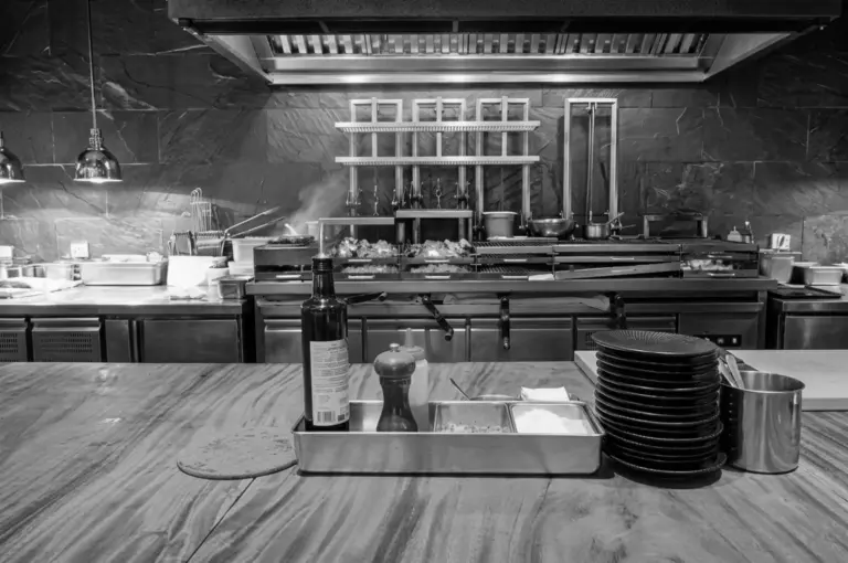 Open kitchen counter view showing grills, cooking equipment, stacked plates, and pendant lights at Burnt Ends