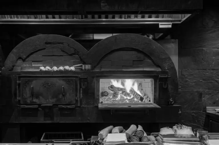 Custom-built dual-cavity wood-fired oven with flames burning and firewood stacked in front