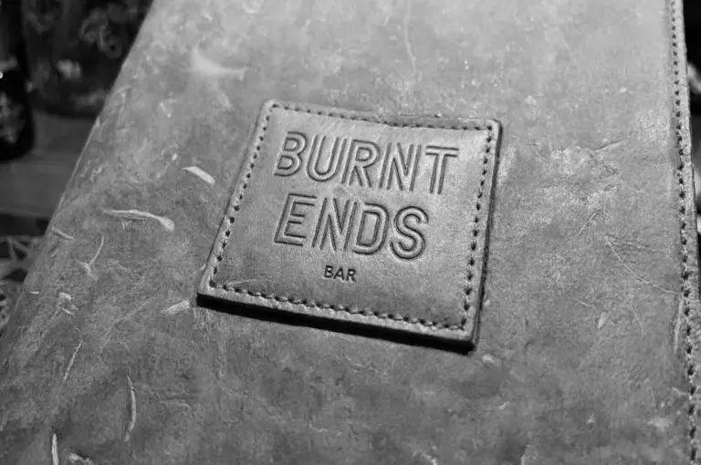 Close-up of leather menu cover with embossed BURNT ENDS BAR logo showing textured material