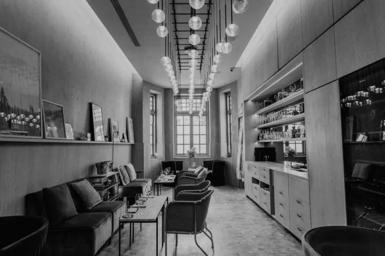 Black and white image of a stylish lounge with modern seating, a long table, wall art, and a ceiling with hanging spherical lights, evoking a cozy, elegant atmosphere.
