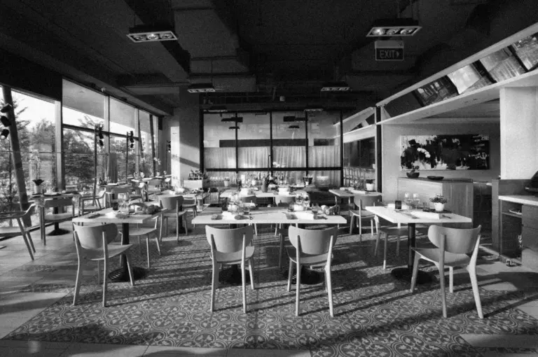 Chic black and white restaurant interior with empty tables and chairs. Large windows let in natural light, highlighting elegant table settings. Calm ambiance.