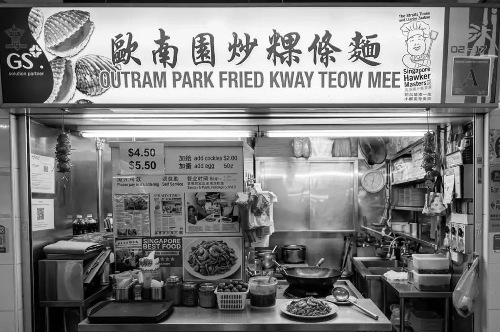 Black and white storefront view of the Outram Park Fried Kway Teow Mee stall showing the signboard and cooking station