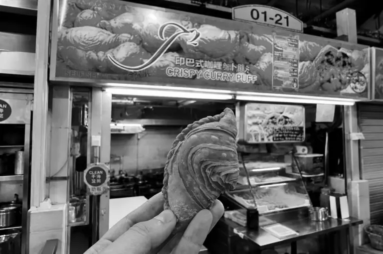 Hand holding crispy curry puff in front of J2 Crispy Curry Puff hawker stall