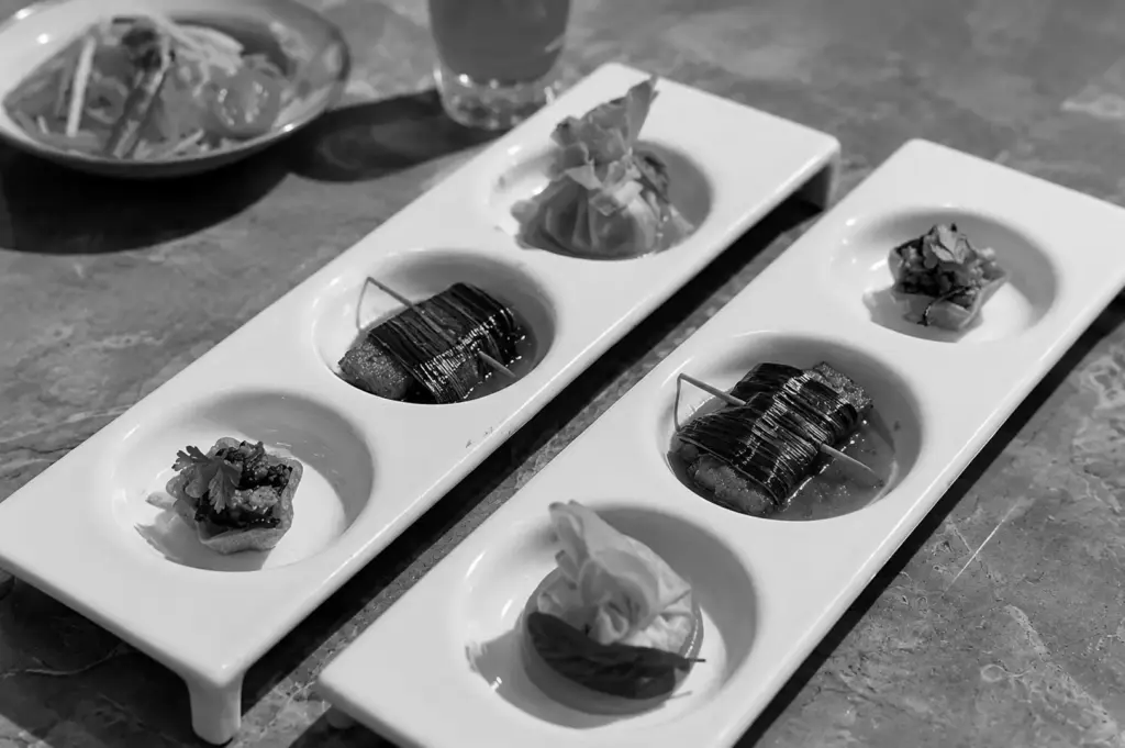 Two long white rectangular plates with three small appetizers each, including wrapped dumplings and leaf-wrapped items