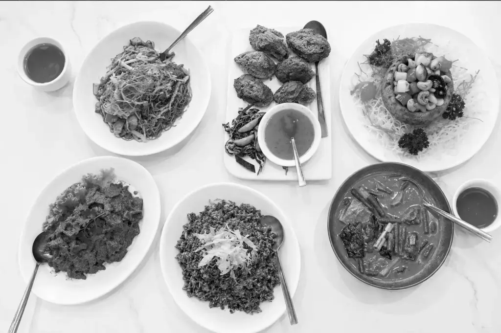 Overhead view of a spread of diverse vegetarian dishes including noodles, rice, and curries on white plates