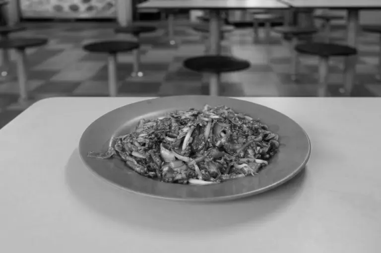 Black and white photo of a plate of Outram Park Fried Kway Teow Mee on a white table in a hawker center