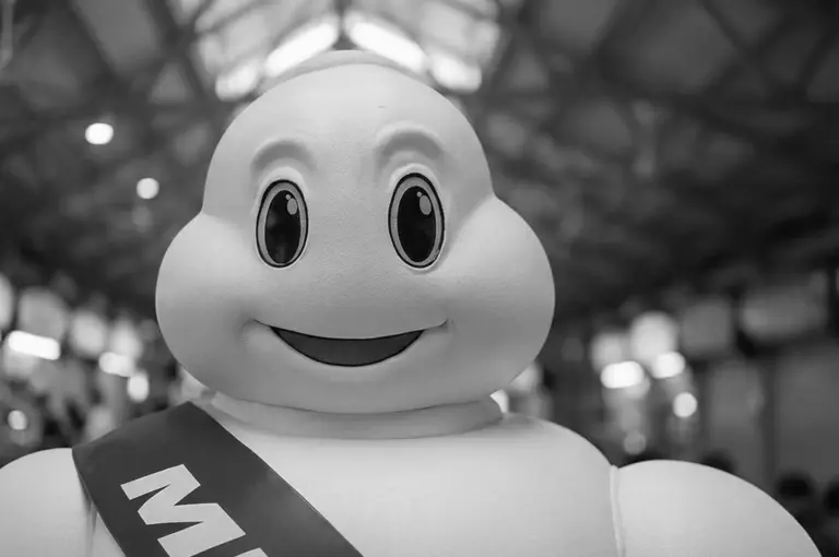Black and white close-up portrait of the smiling Michelin Man mascot wearing a sash