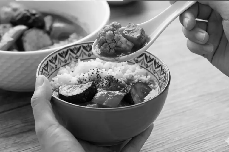 Spoon lifting vegetables from soup curry bowl showing brothy consistency over rice