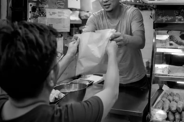 Vendor serving customer with paper bag of curry puffs at food stall counter