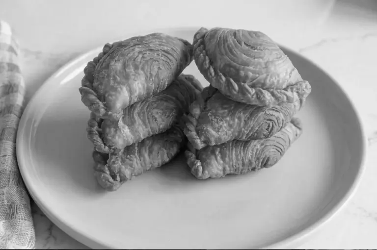 Stack of golden flaky curry puffs arranged on white plate