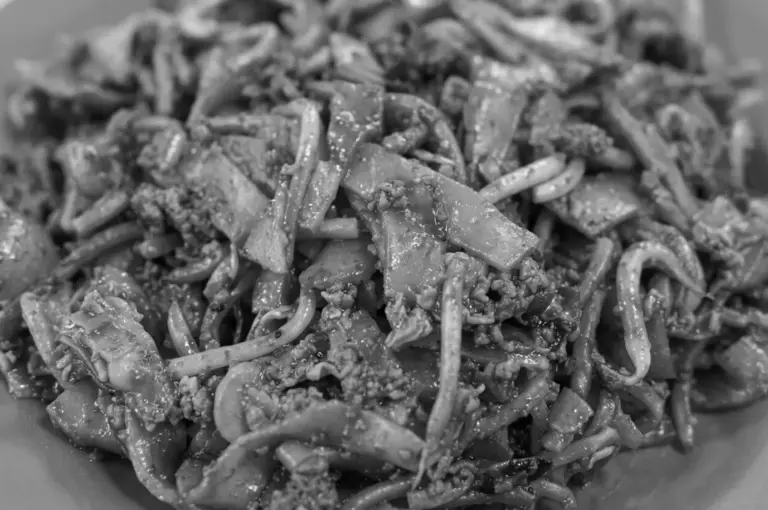 Close-up black and white detail of stir-fried flat rice noodles with cockles and lard