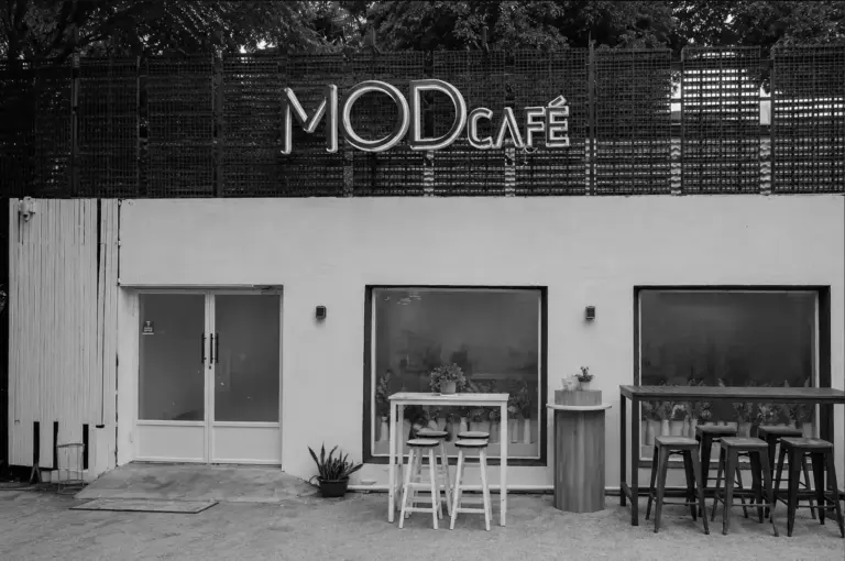 MOD Café exterior featuring a white wall, large windows, and neon signage