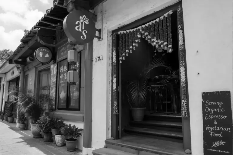 Exterior of AS restaurant with hanging flower garlands at entrance and sign for organic vegetarian food