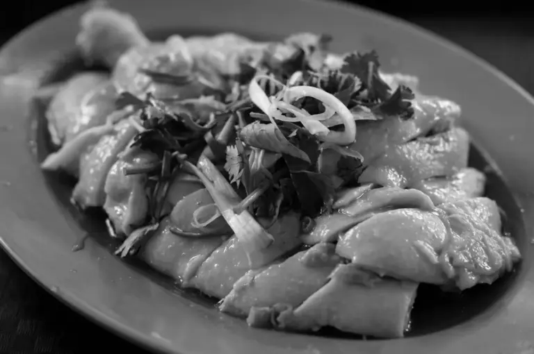 Close-up of tender poached Hainanese chicken slices garnished with fresh cilantro and ginger scallions on a plate