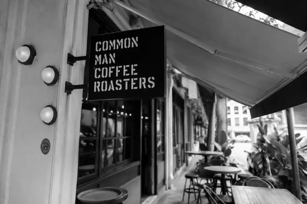 Exterior view of the Common Man Coffee Roasters hanging sign with alfresco seating