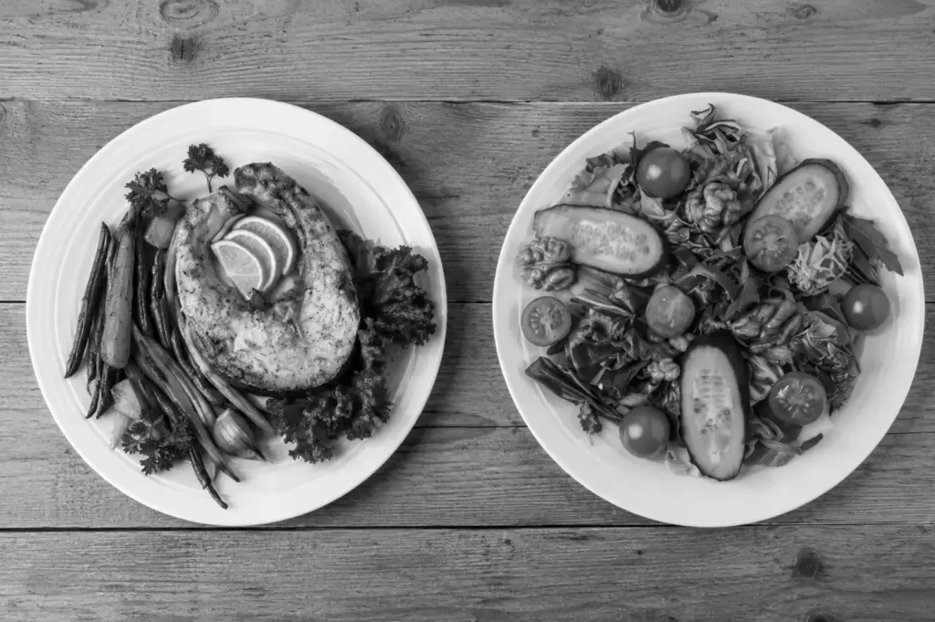 Two plates with grilled fish and fresh salad on wooden table