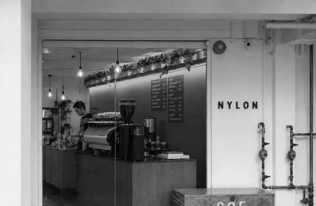 The entrance to Nylon Coffee Roasters features the cafe name on the wall and a view of the barista working at the espresso machine inside