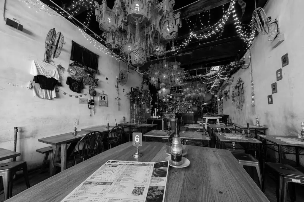 Rustic bohemian cafe interior featuring ornate chandeliers, fairy lights, wooden tables, and eclectic wall decorations with table number and menu visible