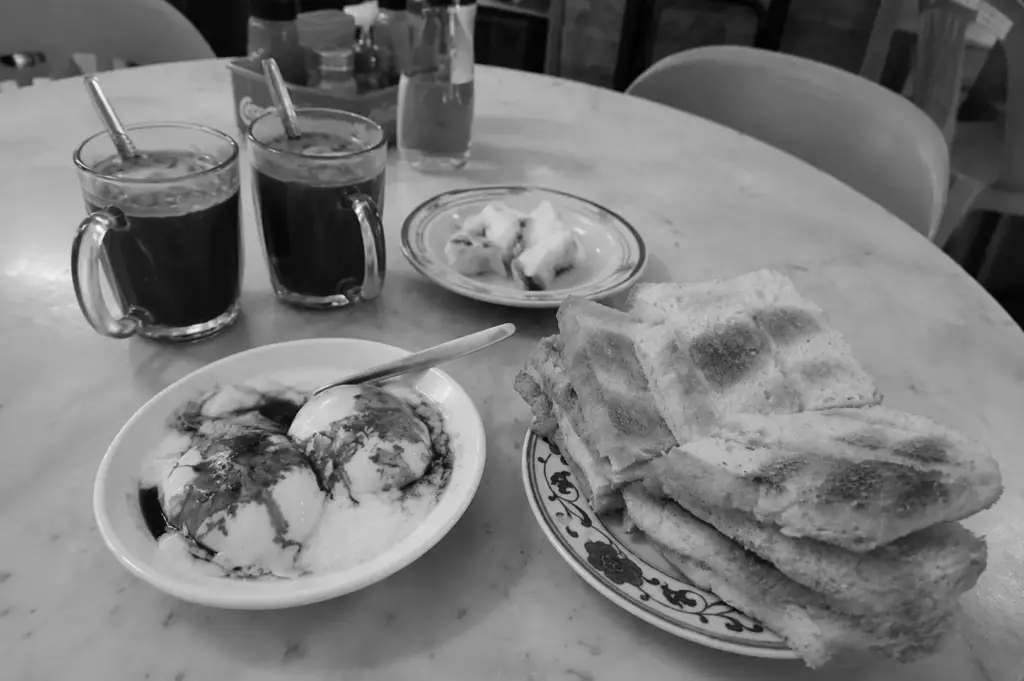 Traditional Singaporean breakfast spread featuring kaya toast, soft-boiled eggs with soy sauce, and two cups of dark coffee