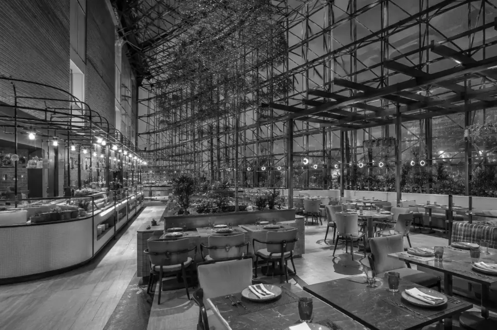 Black and white wide shot of the SKAI restaurant interior featuring a glass atrium ceiling with lush plants and set dining tables