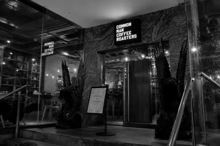 Common Man Coffee Roasters entrance featuring illuminated signage and large winged statues flanking the glass doors