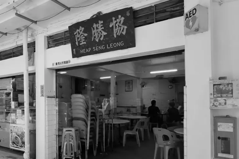 Exterior view of Heap Seng Leong kopitiam with stacked chairs visible inside the open storefront