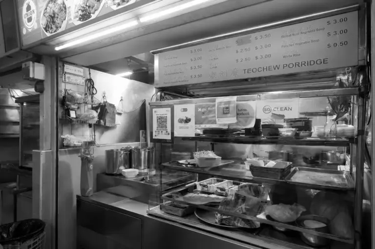 Teochew Porridge hawker stall showing the menu board, stainless steel cooking pots, and food preparation counter