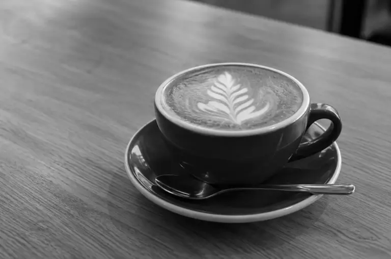 Close-up of a latte with leaf art in a dark cup on a wooden table