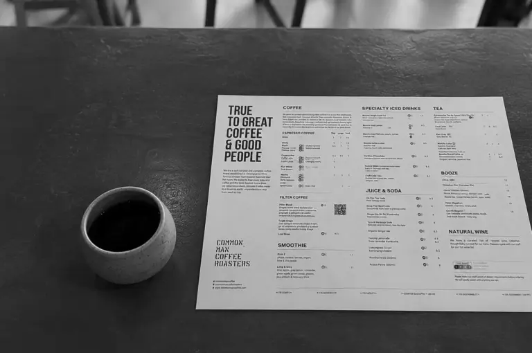Shot of the Common Man Coffee Roasters menu on a dark table next to a black coffee