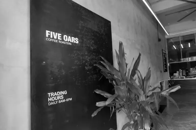 Five Oars Coffee Roasters displaying trading hours, with a large potted plant in the foreground