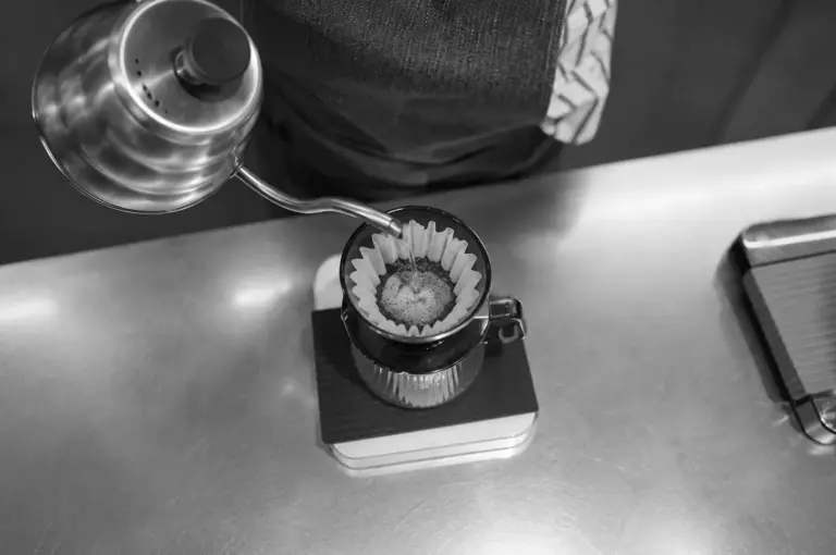 Barista pouring hot water from a gooseneck kettle into a pour-over coffee dripper on a scale