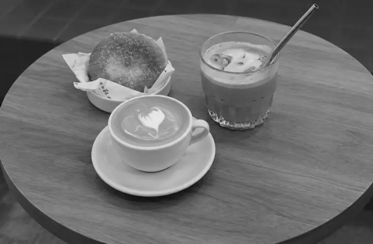 A hot latte with heart art, an iced coffee, and a wrapped pastry are arranged on a round wooden table
