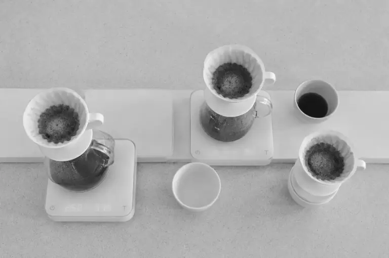 Top-down view of multiple pour-over coffee drippers on digital scales with brewed coffee cups