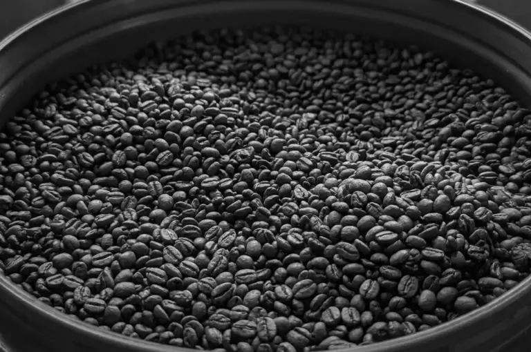 A close-up view of freshly roasted coffee beans filling a large container, captured in black and white