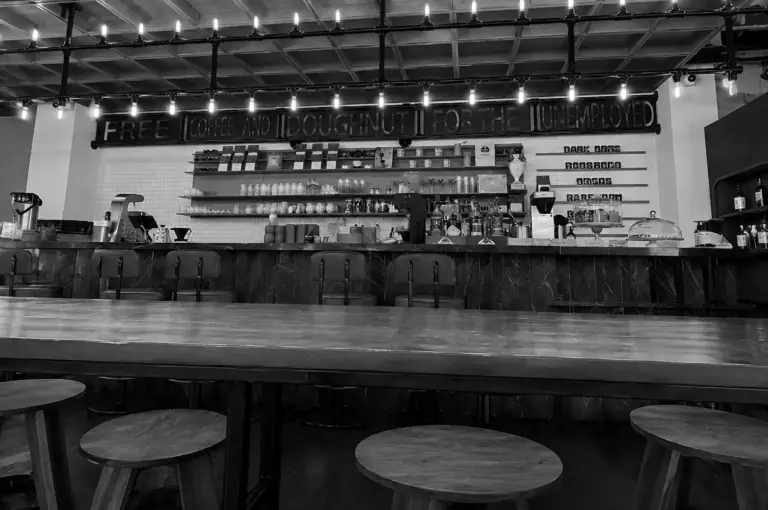 Interior of Common Man Coffee Roasters showing a long communal table and a sign reading free coffee and doughnut for the unemployed