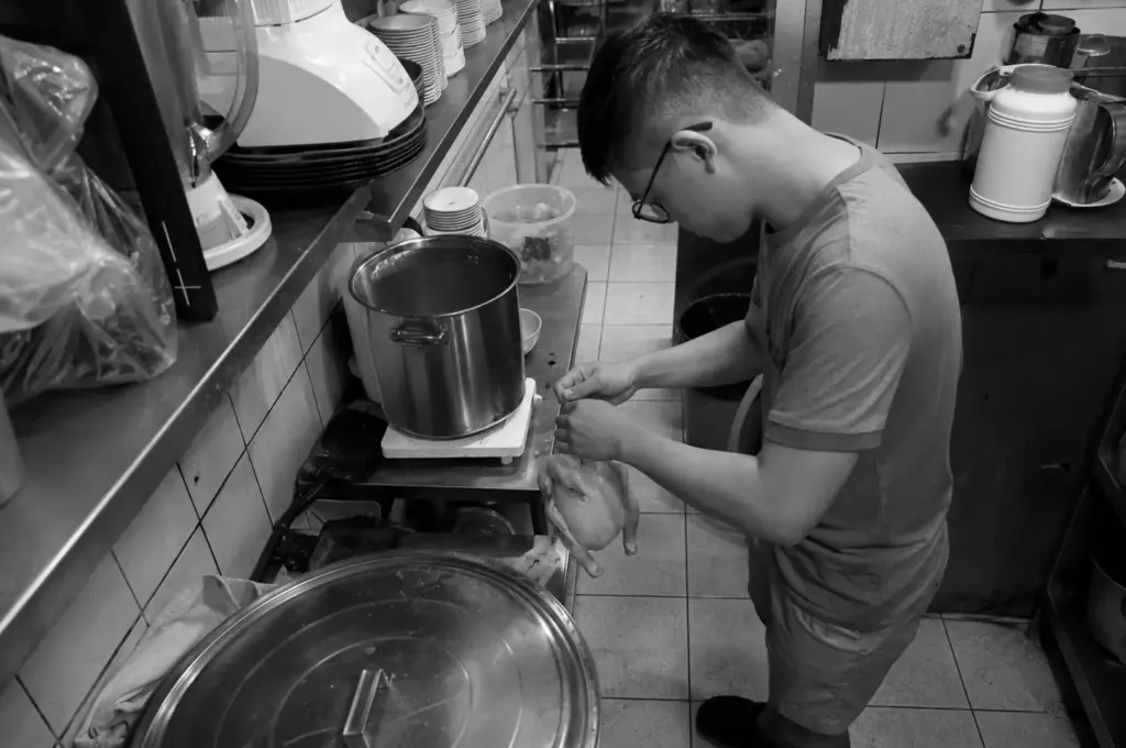 Young hawker carefully preparing fresh ingredients in a compact kitchen, highlighting the dedication of the next generation carrying on Singapore's hawker heritage.