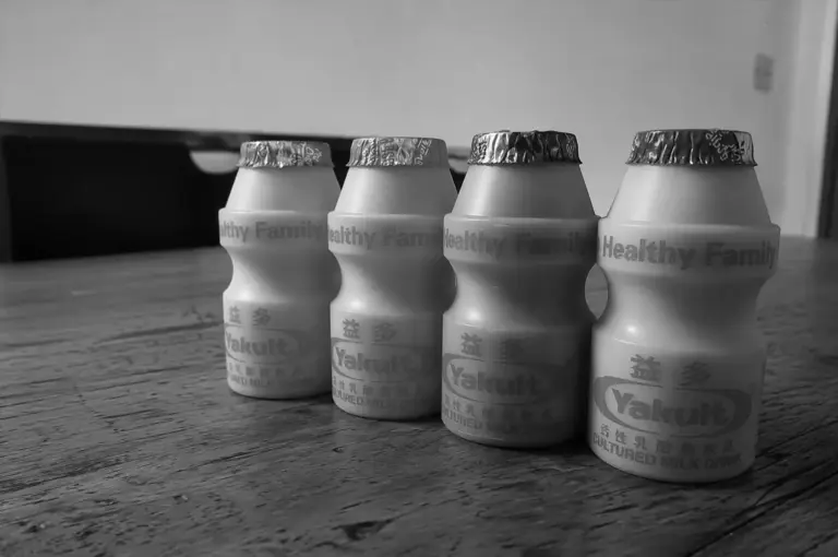 Side-angle view of four Yakult bottles lined up on a wooden table.