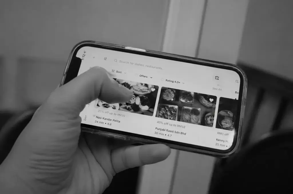 Black-and-white close-up of a person browsing a food discovery app on a smartphone