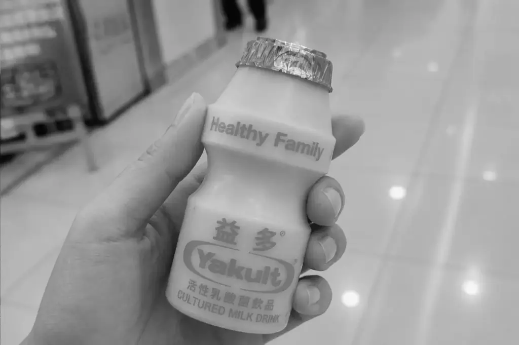 Close-up of a hand holding an orange-flavored Yakult bottle indoors.