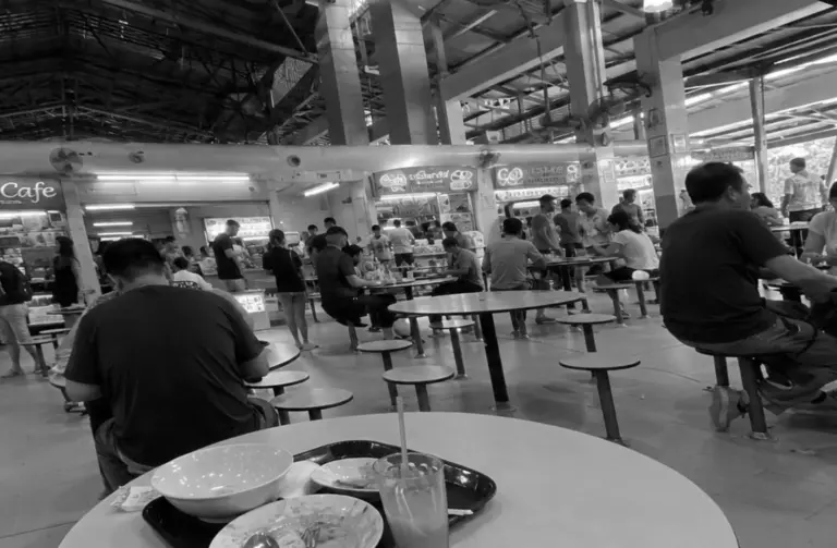 Diners seated in a spacious Singapore hawker centre food court.