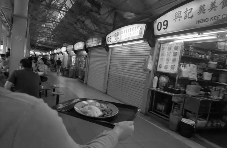 Person carrying a meal tray through a Singapore hawker centre walkway.