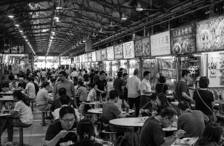 Busy Singapore hawker centre with diners and long rows of food stalls.