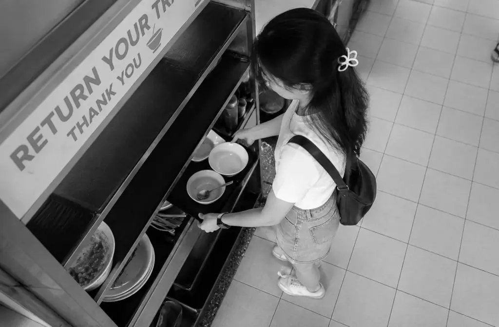 Woman returning used bowls at a hawker centre tray return station.